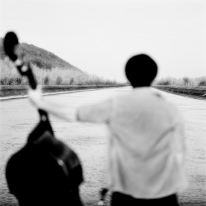 Adam Ben Ezra standing back with his double bass looking to the river horizon.