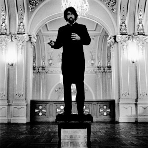 Eivind Gullberg Jensen standing on a chair posing with baton in historic hall.