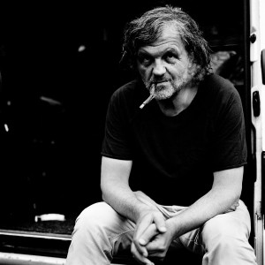 Emir Kusturica sitting and smoking a cigarette.