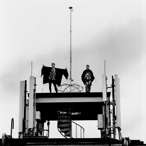 Gus Gus members Daniel Agust Haraldsson and Birgir Porarinsson posing on a broadcaster at the rooftop of the building with skies in the background.