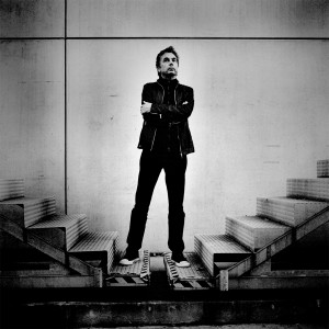 Jean-Michel Jarre standing between two stairways with his hands crossed on his chest.