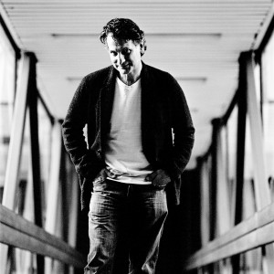 John Patitucci standing in a glass corridor with one hand in his pocket.