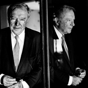 Krzysztof Zanussi posing at a mirror with his own reflection wearing a suit.