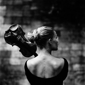 Mari Samuelsen from the back holding violin with brick wall in the background.
