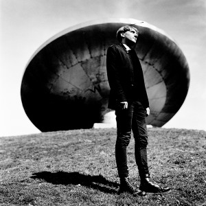 Cyborg artist Neil Harbisson standing in front of ufo spaceship monument.