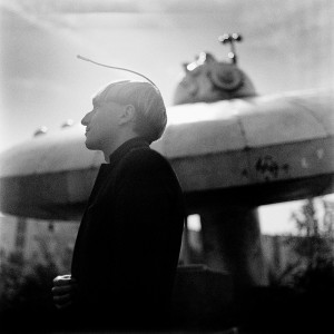 Cyborg artist Neil Harbisson standing in front of ufo spaceship monument.