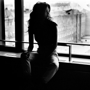 Samar Qupty sitting on railing of a balcony with houses and street in the background.