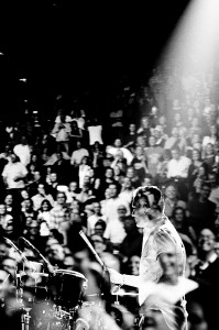 Double exposure of U2 drummer Larry Mullen Jr. playing drums with the people in the audience.