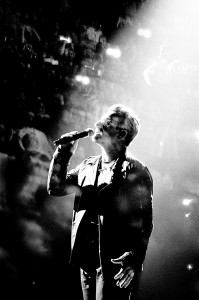 Double exposure of U2 frontman Bono Vox singing to the microphone with the audience.