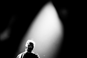 U2 frontman Bono Vox standing back on the stage in the light at the concert.